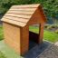Nature Playhouse vyrobený z dřevěných prken v travnaté zahradě.
