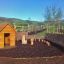 Nature Playhouse v přírodním venkovním prostředí s dřevěnými herními prvky a proutěným oplocením.