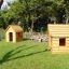Dvě dřevěné konstrukce Nature Playhouse na trávě se stromy v pozadí.