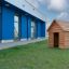 Dřevěný Nature Playhouse na travnatém trávníku před moderní modrou budovou.