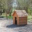 Dřevěný Nature Playhouse v parku s houpačkou v pozadí.