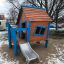 Olle's Playhouse dřevěný domeček na hraní s modrými prvky a skluzavkou ve sněhovém parku.