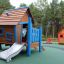 Dřevěný domeček na hraní s modrými prvky a skluzavkou na hřišti s názvem Olle's Playhouse.